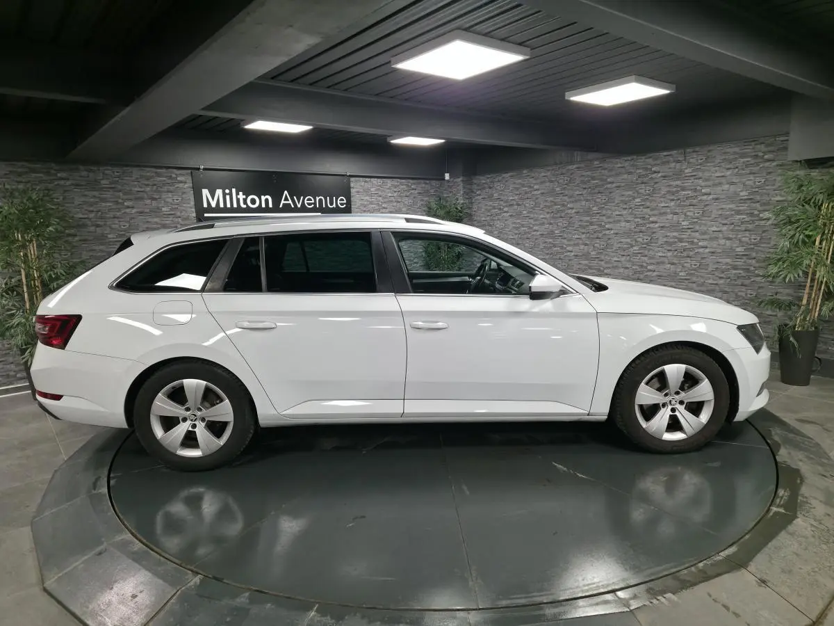 Profil droit d'un break SKODA SUPERB blanc 2018 sur plateau tournant en intérieur avec jantes alliage 5 branches.