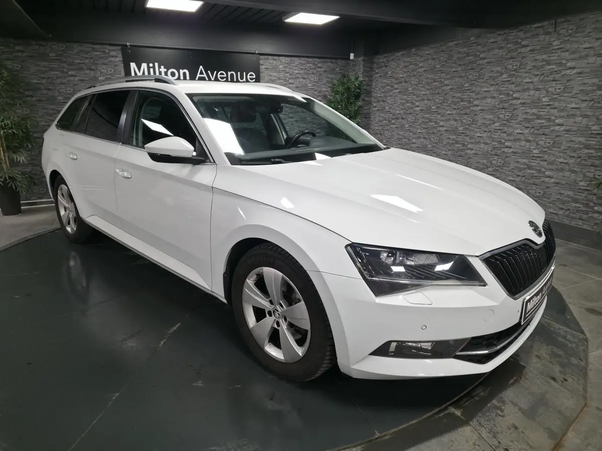 Vue 3/4 avant gauche d'un break Skoda Superb blanc avec jantes alliage 17 pouces dans un showroom.