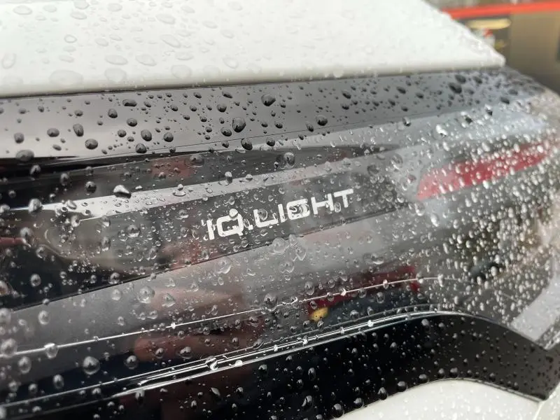 Gros plan sur le feu arrière noir brillant avec inscription iQ.LIGHT du Volkswagen Tiguan blanc, couvert de gouttes de pluie.