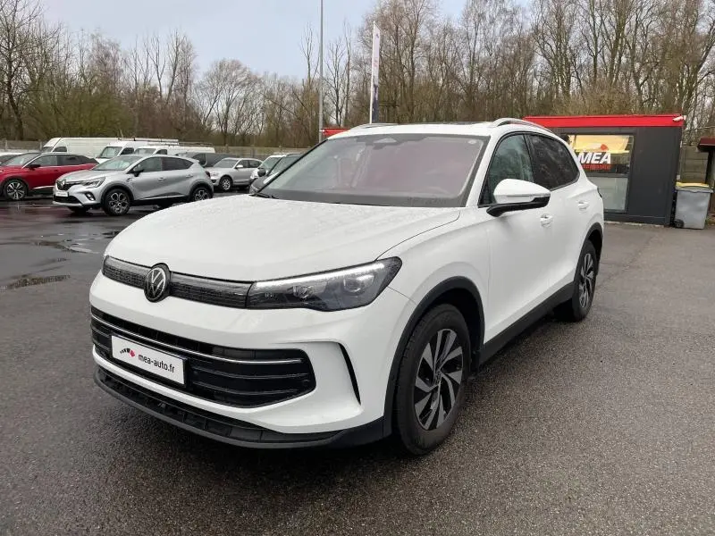 Volkswagen Tiguan blanc Pur en 3/4 avant droit sur parking humide avec jantes alu et toit ouvrant panoramique visible.