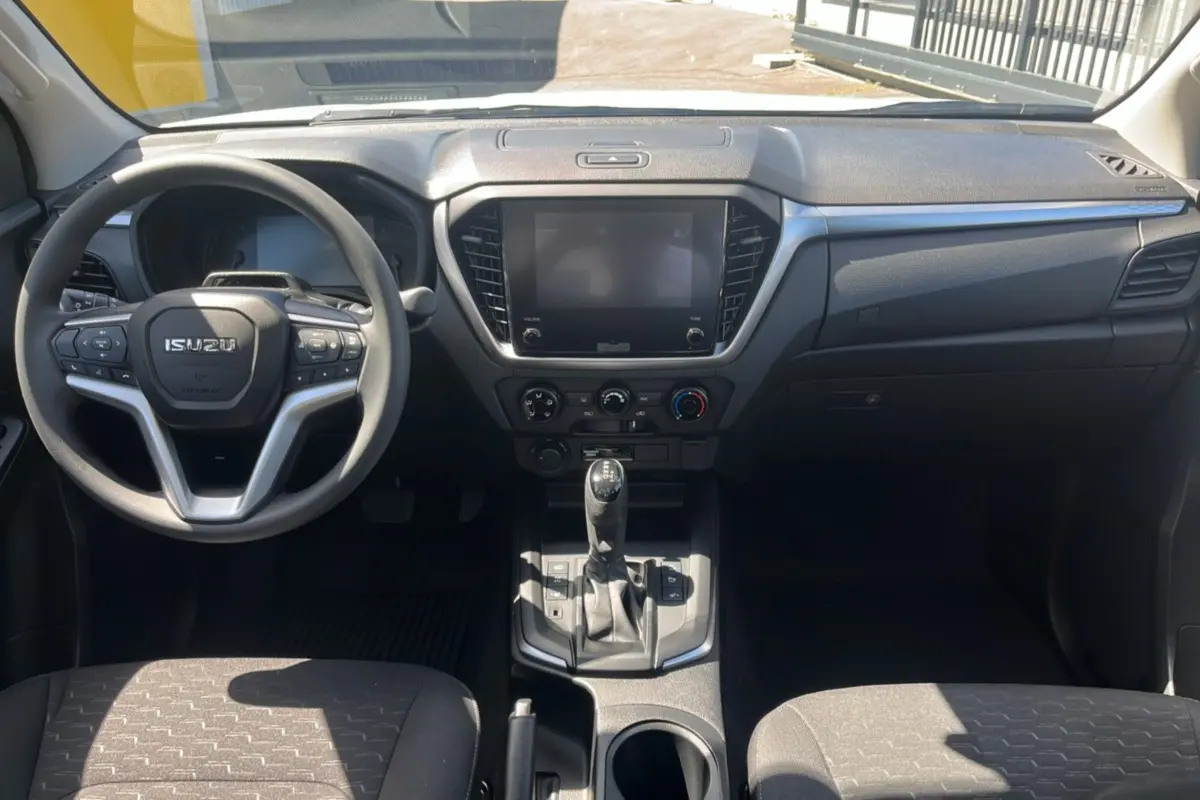 Vue intérieure avant de l'Isuzu D-MAX 2026 avec tableau de bord noir, volant multifonctions et écran tactile central éteint.