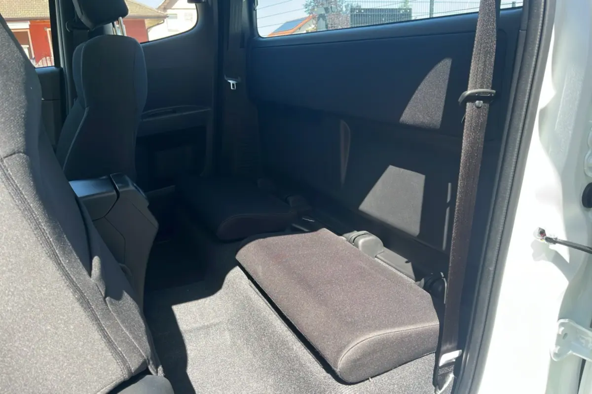 Vue intérieure arrière côté droit du pick-up Isuzu D-MAX 2.2 TD 164 Space Evolution A/T8 en blanc Splash, sièges arrière rabattus.