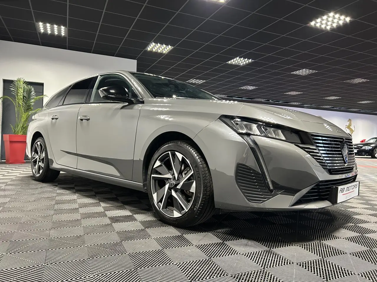 Peugeot 308 SW gris Sélénium vue 3/4 avant avec calandre noire et jantes alliage 17 pouces en intérieur showroom.