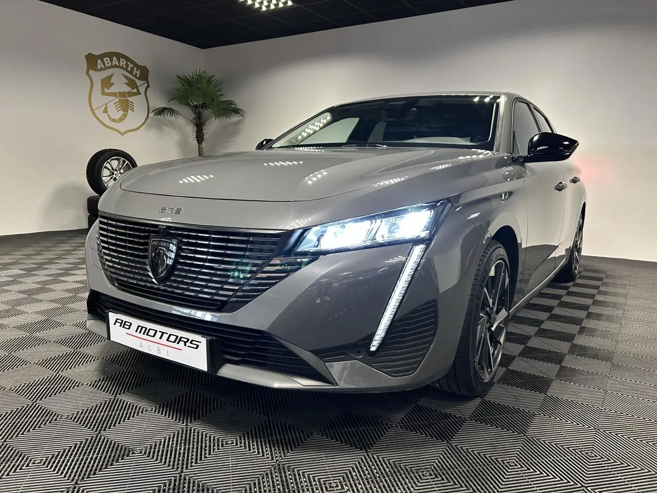 Peugeot 308 SW gris Sélénium vue 3/4 avant droit avec feux LED allumés et jantes alliage noires.