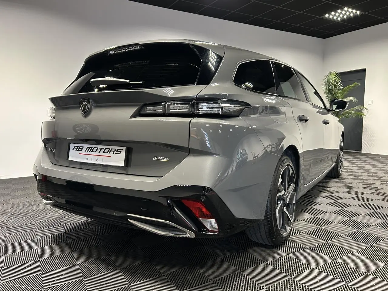 Peugeot 308 SW hybride gris Sélénium vue 3/4 arrière droit en intérieur avec jantes alliage 17 pouces.