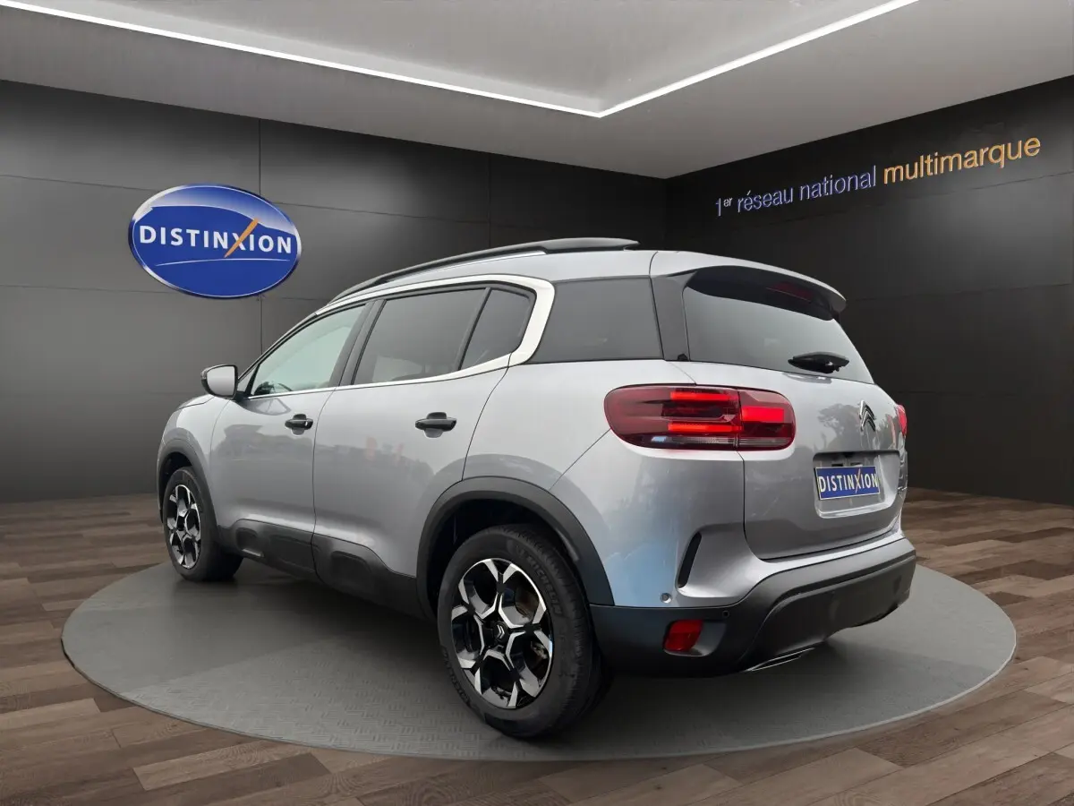 Vue 3/4 arrière droite du Citroën C5 Aircross hybride gris clair avec jantes noires et toit noir en showroom.