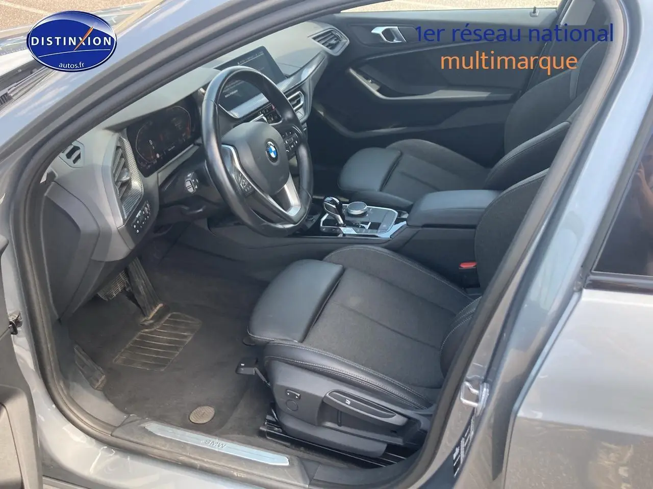 Intérieur côté conducteur d'une BMW Série 1 gris foncé 2023, mettant en valeur les sièges sport et le volant multifonction cuir.