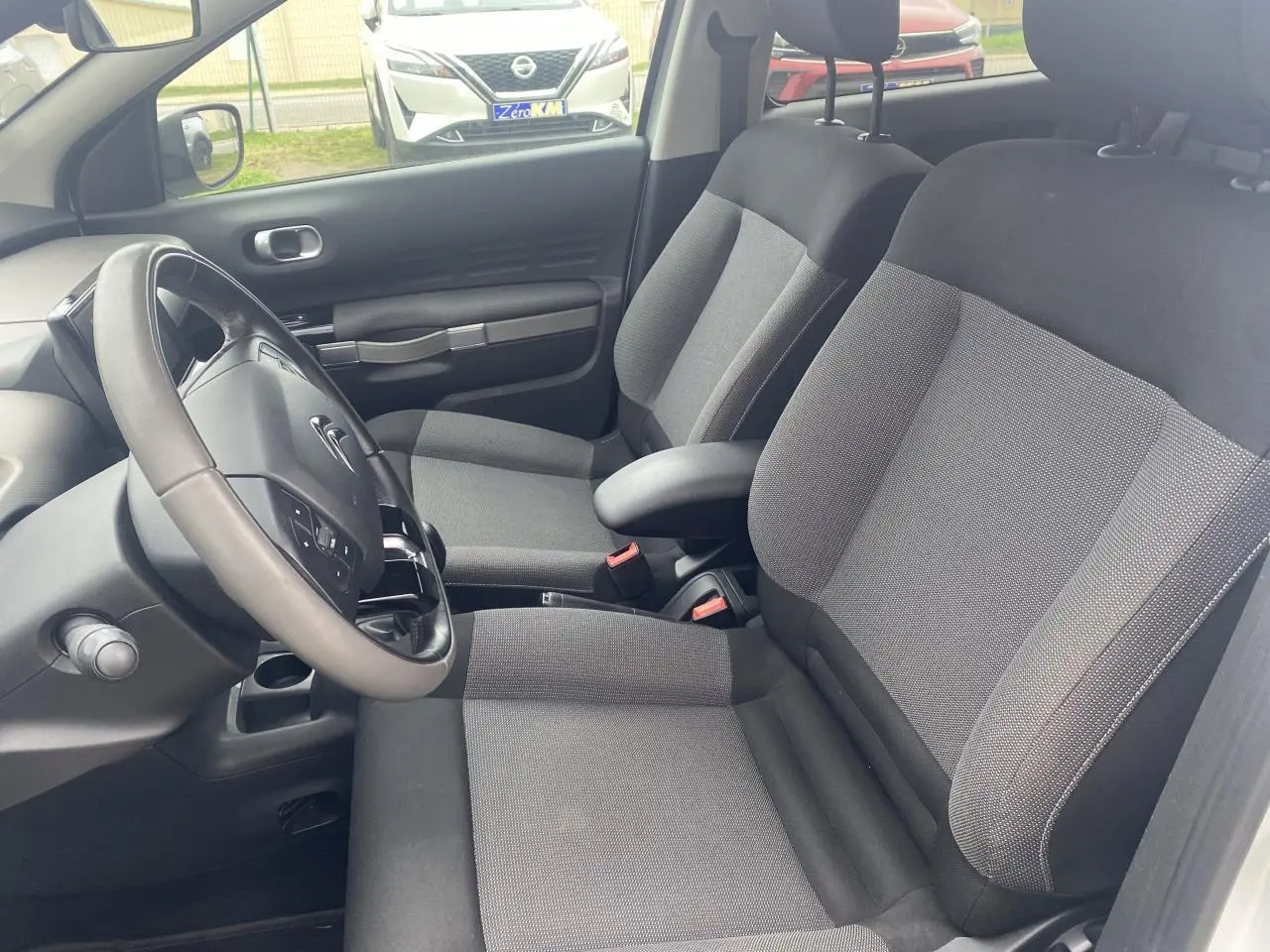 Intérieur avant de la Citroën C4 Cactus blanc, sièges gris avec accoudoir central et volant multifonction.