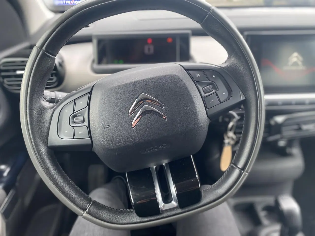 Vue rapprochée du volant noir de la Citroën C4 Cactus 2015 avec commandes intégrées et tableau de bord en arrière-plan.