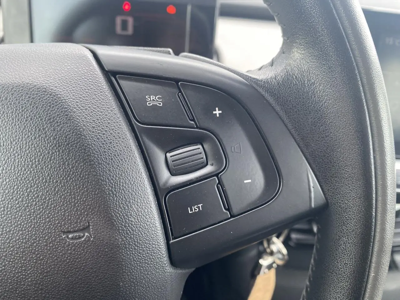 Gros plan sur les commandes gauche du volant noir du Citroën C4 Cactus 2015 essence blanc, intérieur moderne.