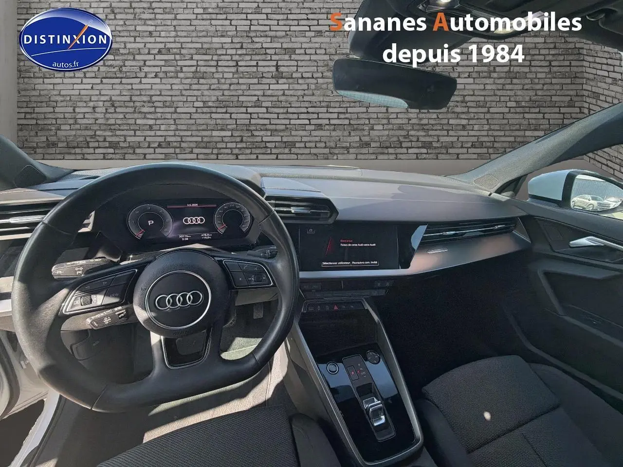 Vue intérieure avant de l'Audi A3 Sportback blanche 2023, mettant en valeur le volant cuir multifonctions et le tableau de bord digital.