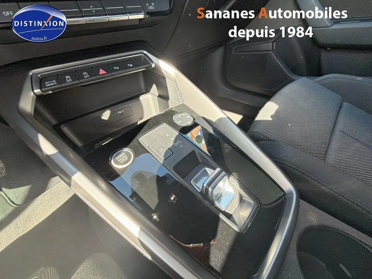 Vue rapprochée de la console centrale noire brillante de l'Audi A3 Sportback 2023 avec levier de boîte auto et boutons multifonctions.