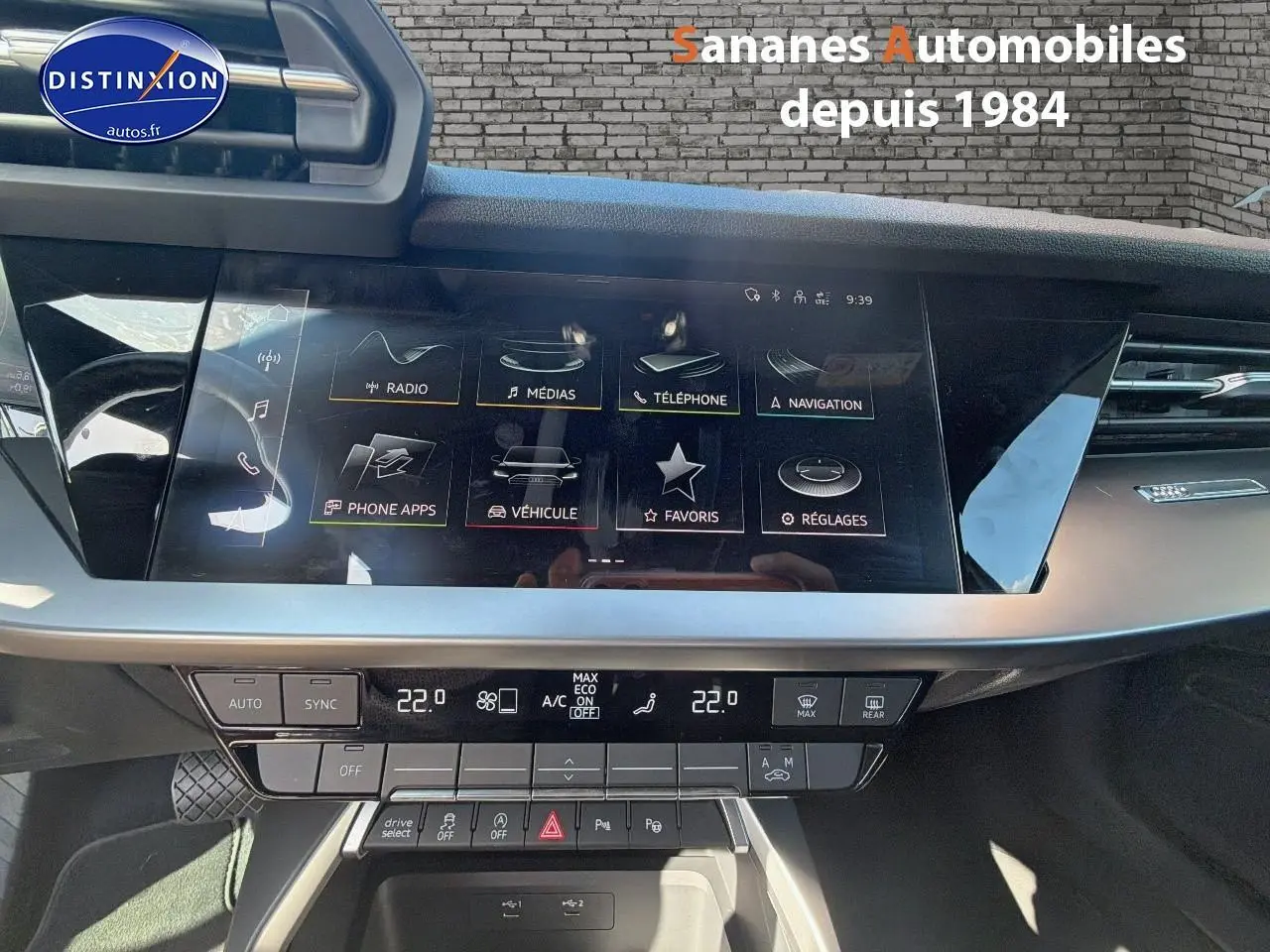 Vue intérieure du tableau de bord de l'Audi A3 Sportback blanc 2023 avec écran tactile et commandes climatisation.