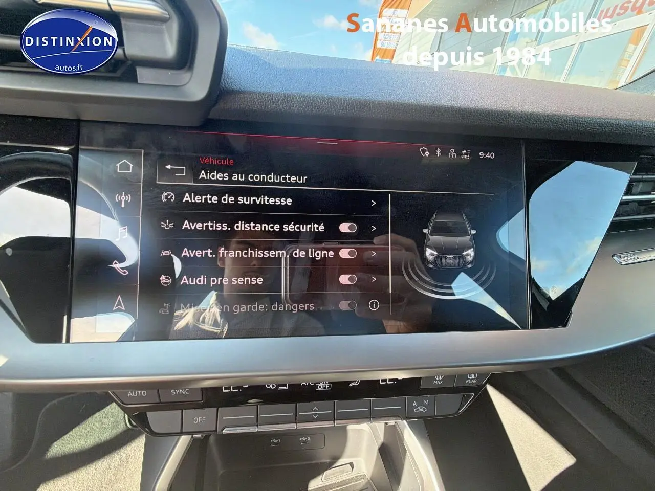 Écran tactile central affichant les aides à la conduite dans l’habitacle d’une Audi A3 Sportback blanche, vue de face.