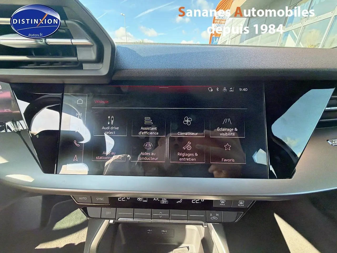 Vue rapprochée de l’écran tactile central noir brillant de l’Audi A3 Sportback blanc, affichant les options de conduite et confort.