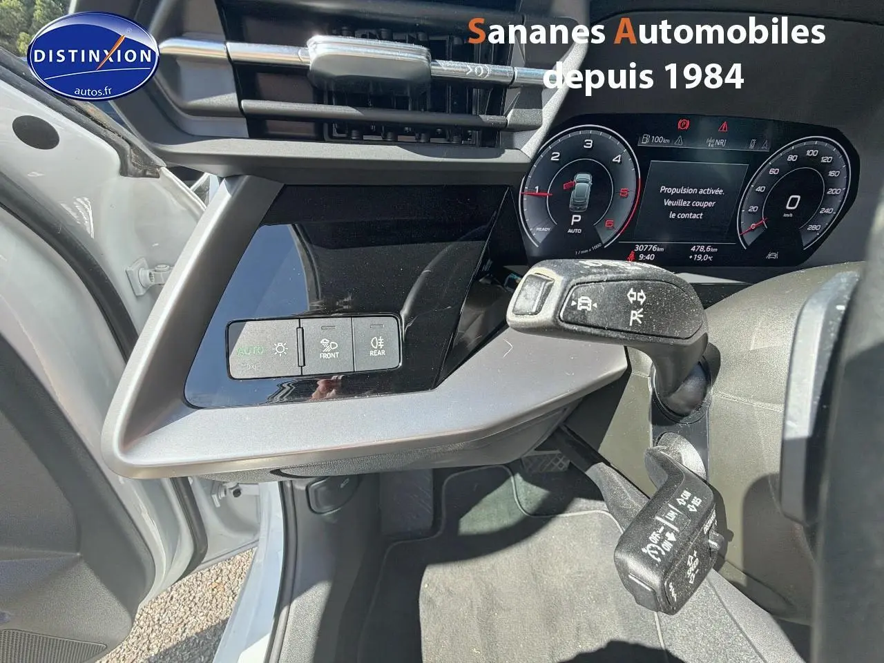 Vue intérieure côté conducteur de l'Audi A3 Sportback blanche 2023, montrant le tableau de bord digital et commandes au volant.