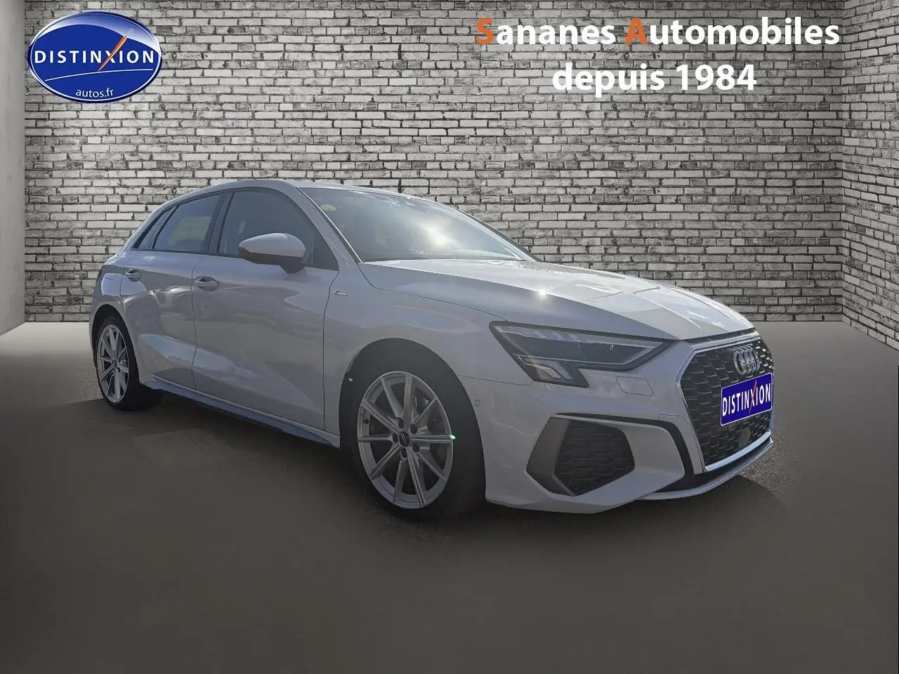 Audi A3 Sportback blanc vue 3/4 avant droit avec jantes alliage et calandre S line devant un mur en briques.