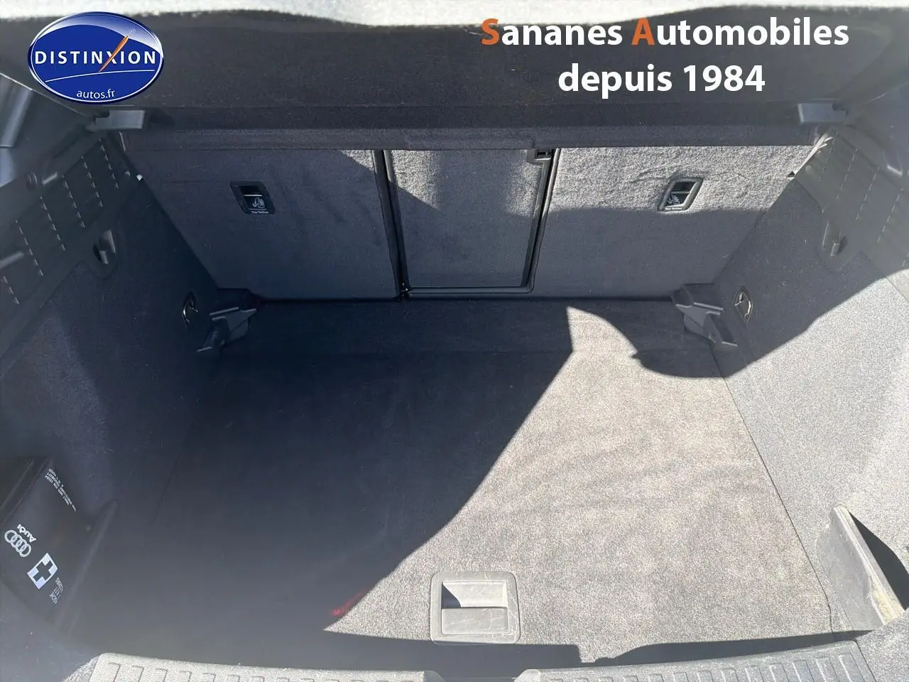 Coffre spacieux et propre d'une Audi A3 Sportback blanche, vue de dessus avec moquette noire et rangements latéraux.