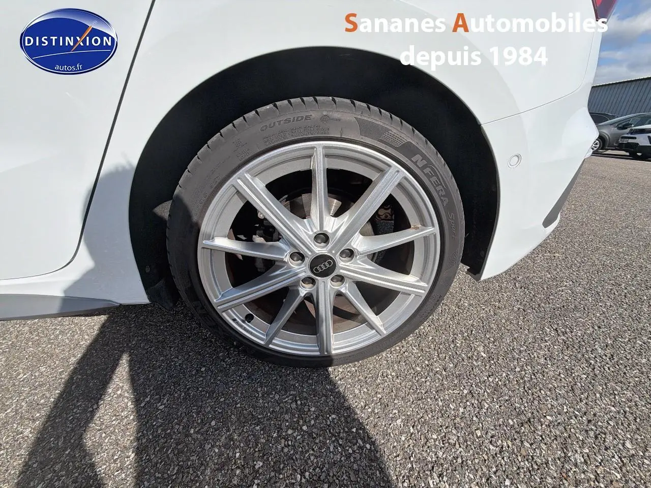 Gros plan sur la roue avant droite en alliage de l'Audi A3 Sportback blanche, avec jante S line visible.