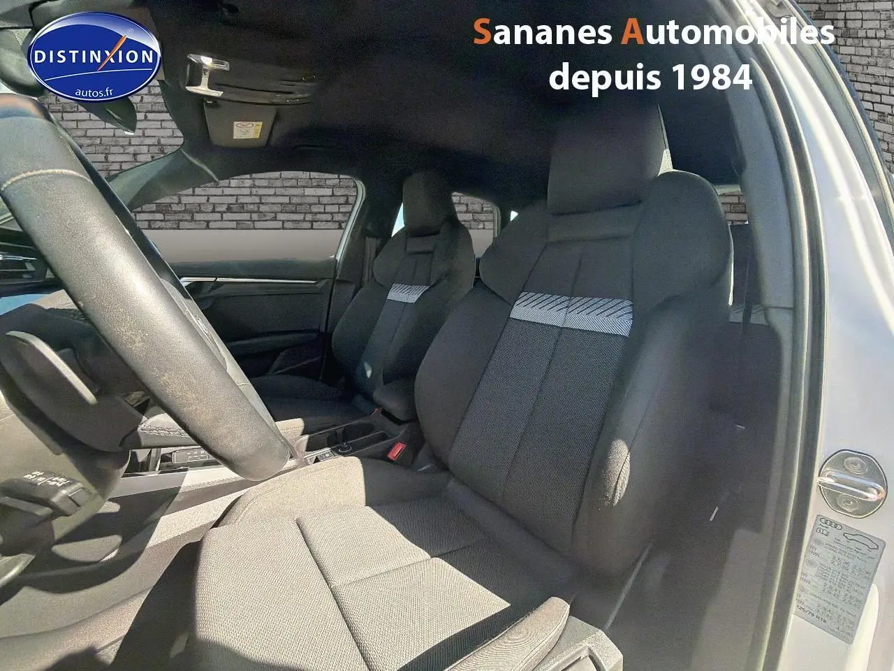 Vue intérieure côté conducteur de l'Audi A3 Sportback blanche, mettant en valeur les sièges sport et le volant cuir multifonctions.