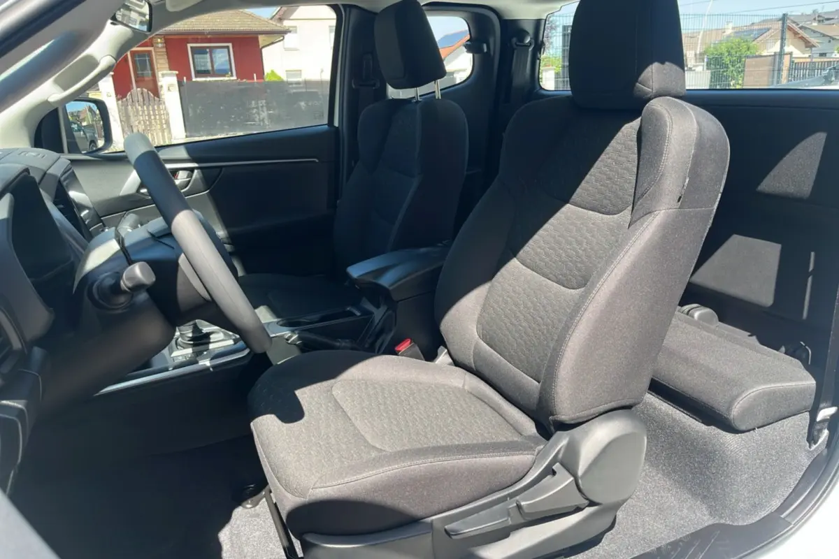 Vue intérieure côté conducteur du pick-up Isuzu D-MAX 2.2 TD 164 Space Evolution, sièges tissu gris et accoudoir central.