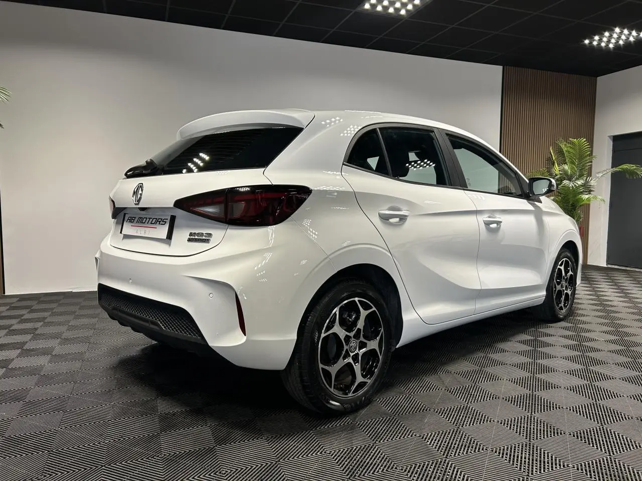 Vue 3/4 arrière droite d'une MG3 1.5 Hybrid+ blanche avec jantes alliage noires et feux arrière fumés.