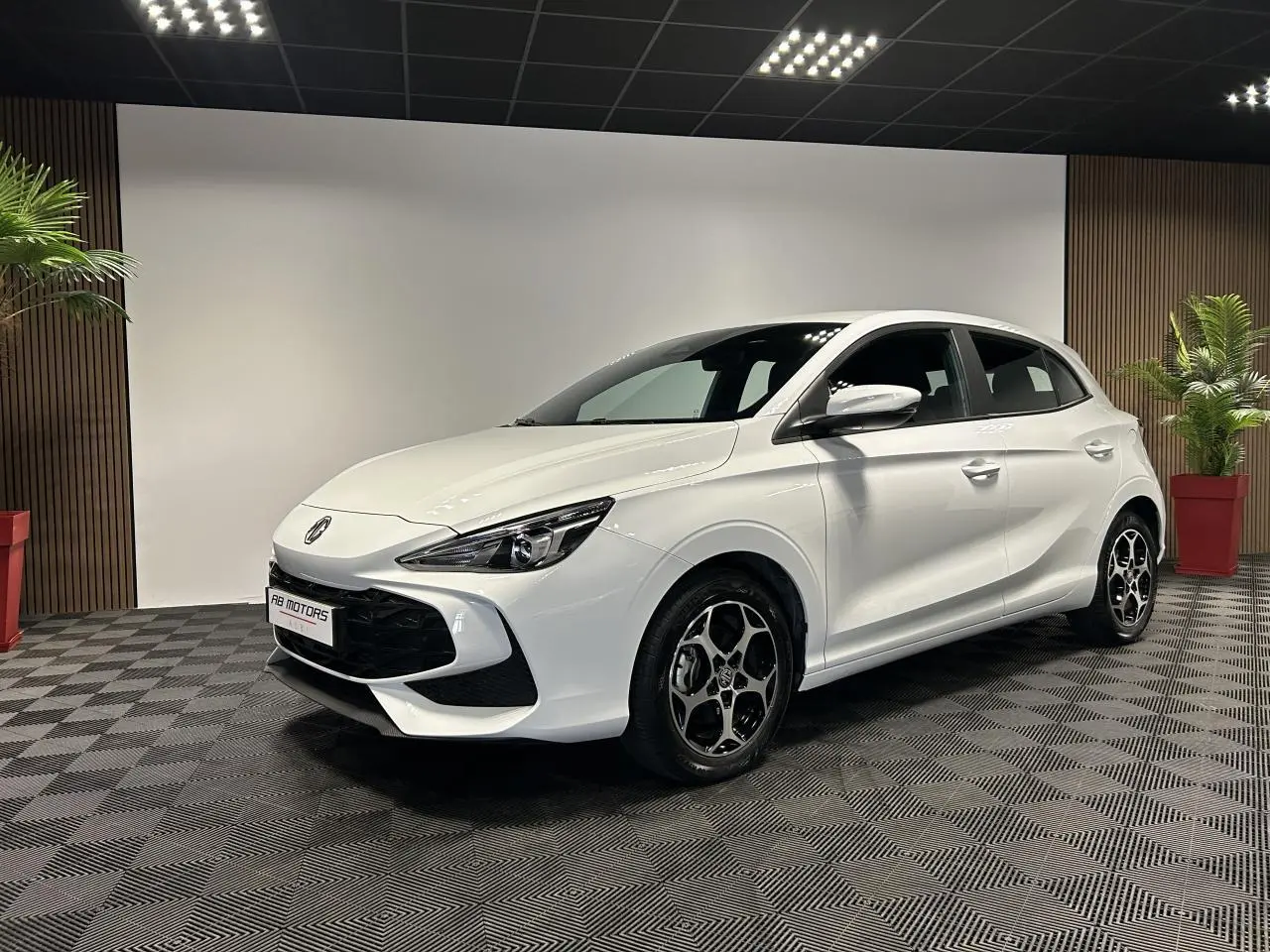 Vue 3/4 avant droite d'une MG3 blanche 2025 avec jantes alliage et calandre noire dans un showroom.