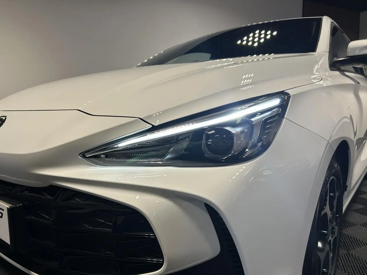 Vue 3/4 avant droit du MG3 blanc 2025 avec phares LED allumés et jantes alliage noires.