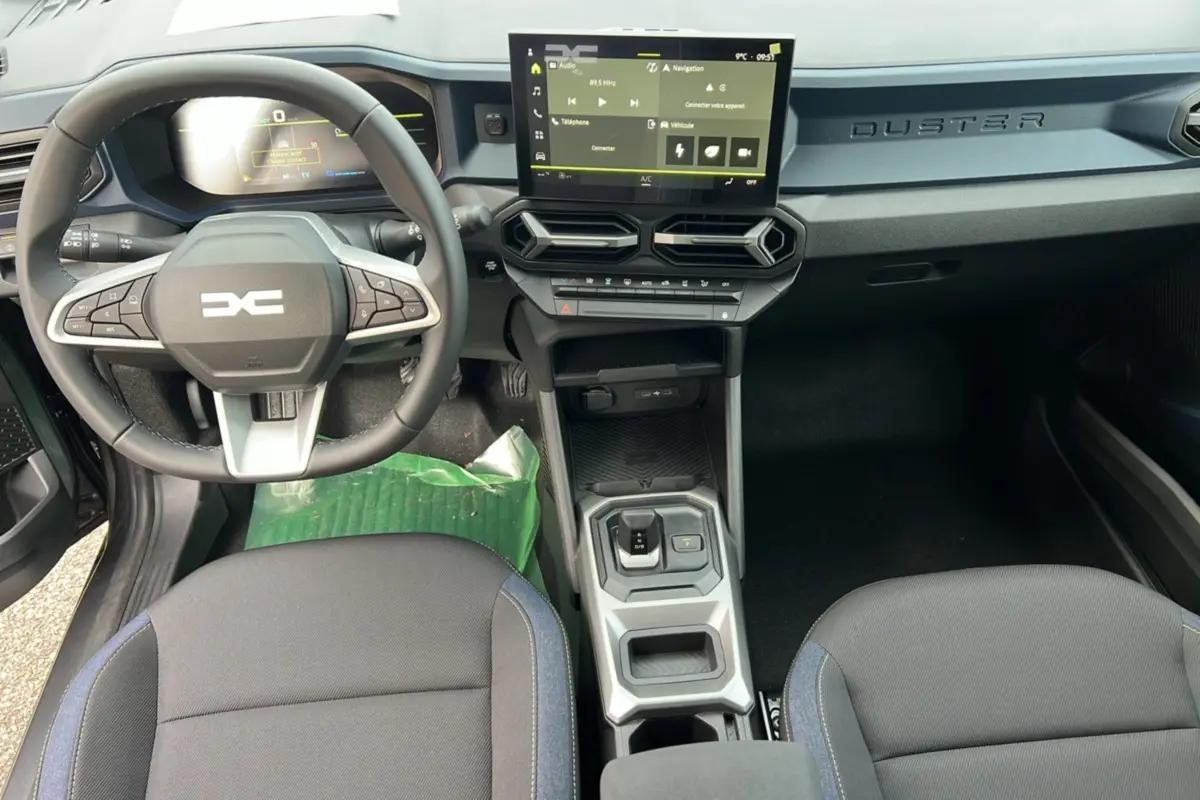 Vue intérieure du tableau de bord et console centrale du Dacia Duster HEV 140 Journey Pack City 2025 avec écran tactile et volant multifonction.
