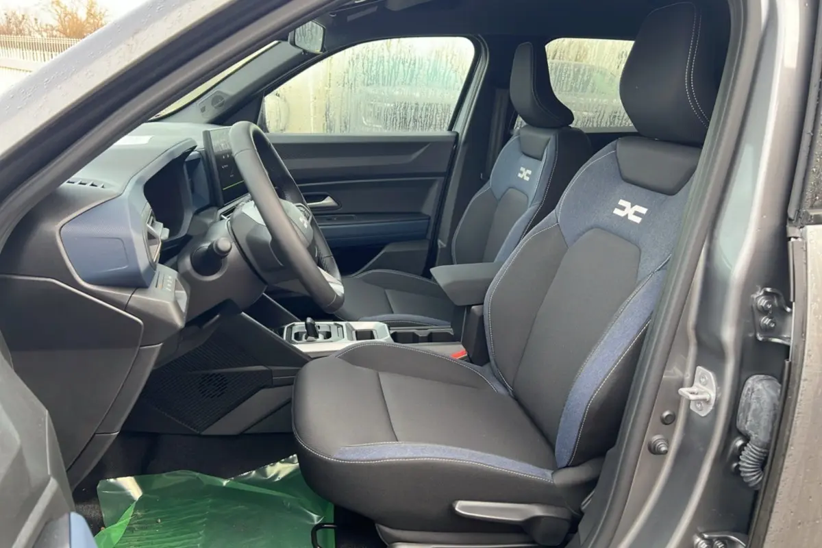 Intérieur côté conducteur du Dacia Duster 2025 noir nacré, sièges tissu avec logo HEV et tableau de bord moderne.