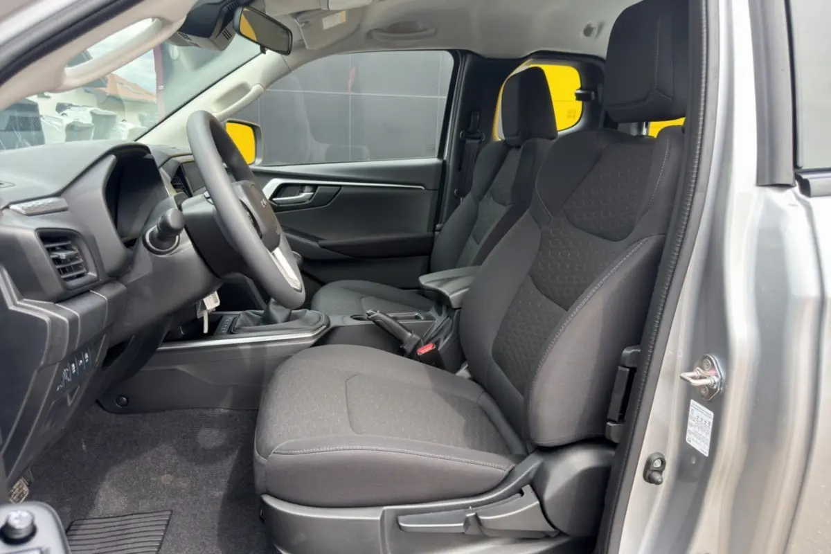 Vue intérieure côté conducteur de l'Isuzu D-MAX 2.2 TD 164 Space Evolution avec sièges tissu gris et accoudoir central.