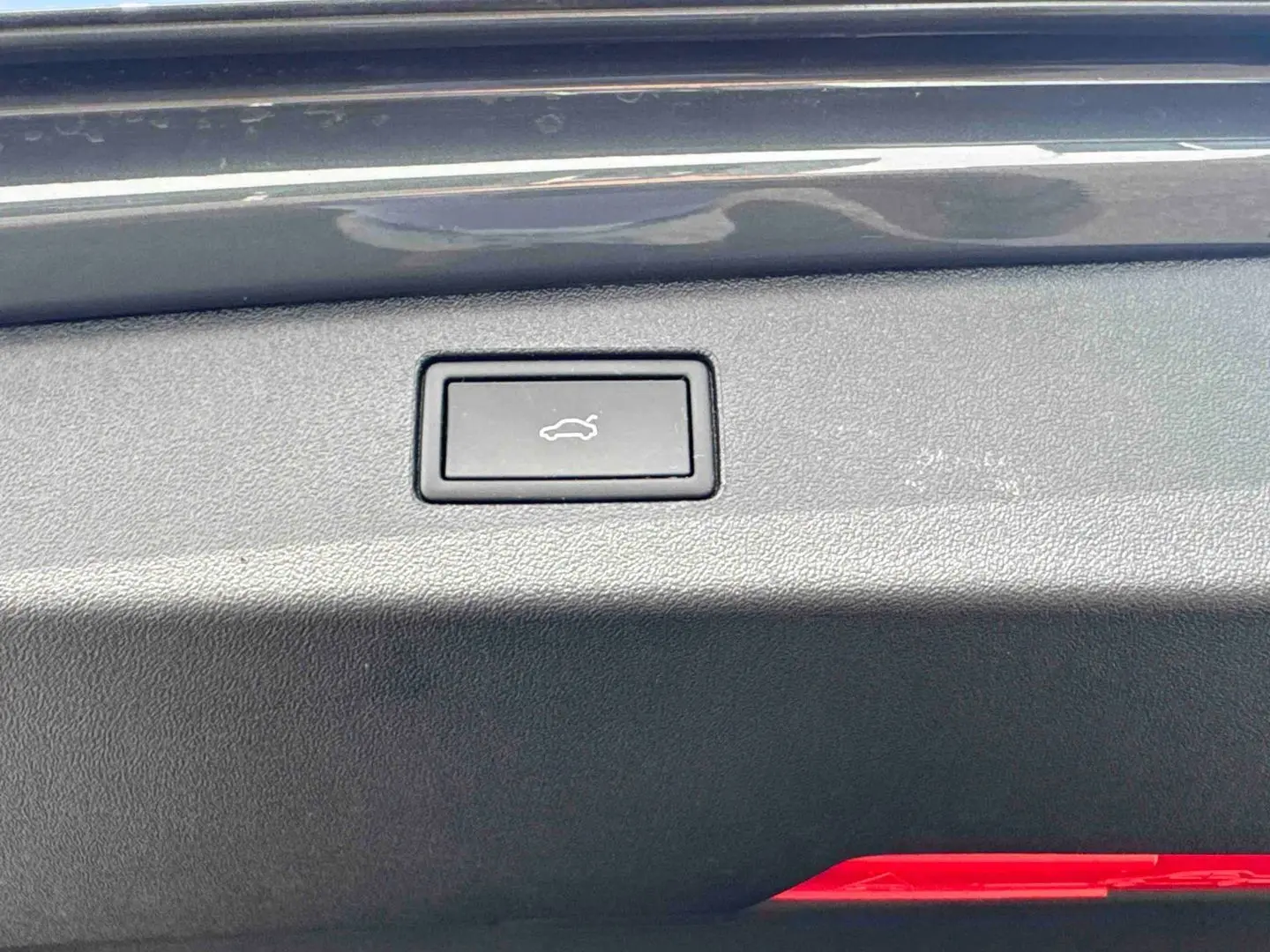 Bouton d'ouverture électrique du coffre sur la plage arrière d'un Volkswagen Tiguan gris, vue intérieure rapprochée.