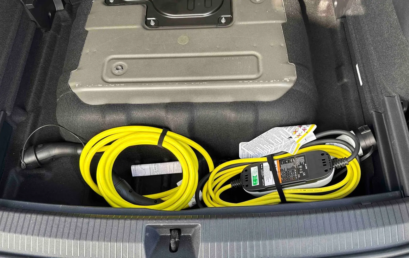 Coffre ouvert d’un Volkswagen Tiguan gris 2025 montrant un câble de recharge électrique jaune rangé.