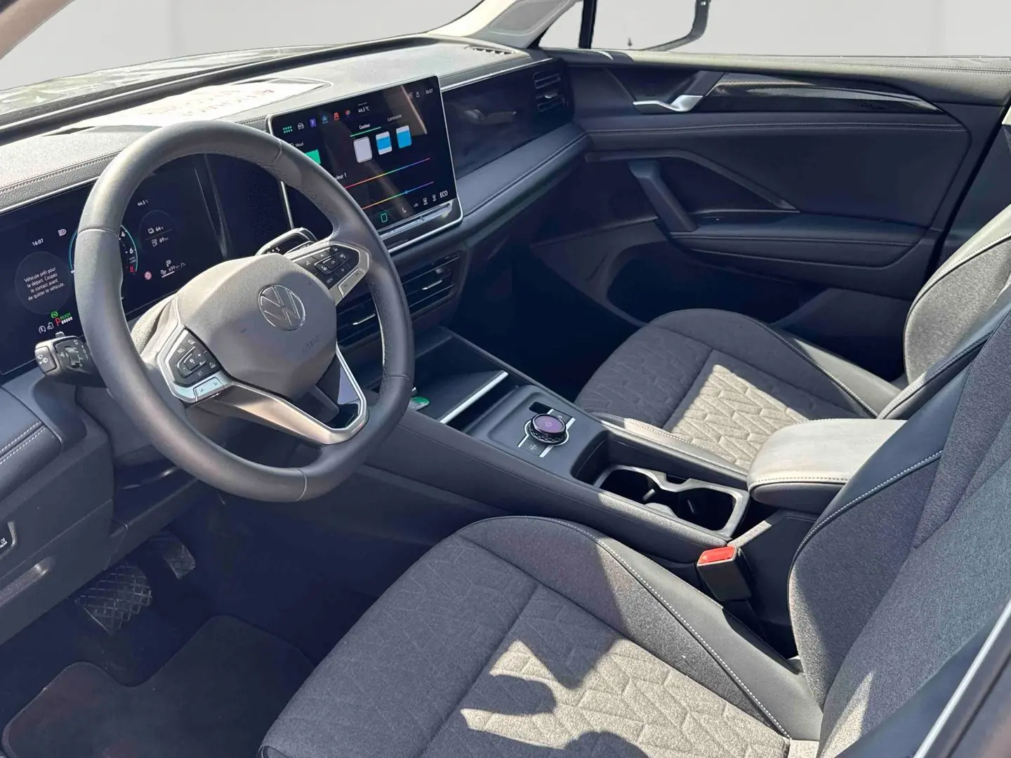 Vue intérieure côté conducteur du Volkswagen Tiguan eHybrid 2025, avec tableau de bord numérique et sièges gris tissu.