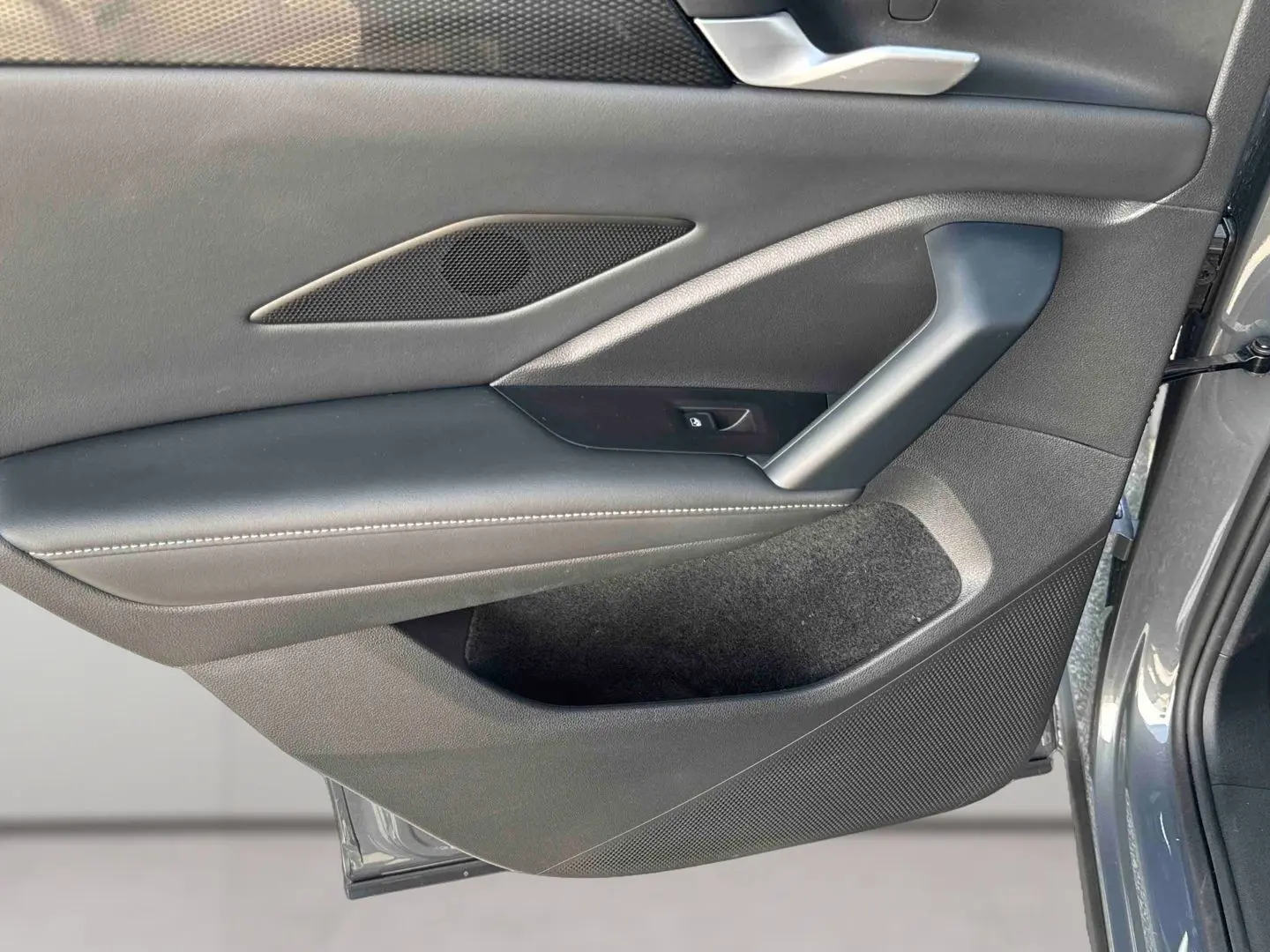 Gros plan sur la porte intérieure côté gauche du Volkswagen Tiguan gris, montrant les commandes et le revêtement en cuir noir.