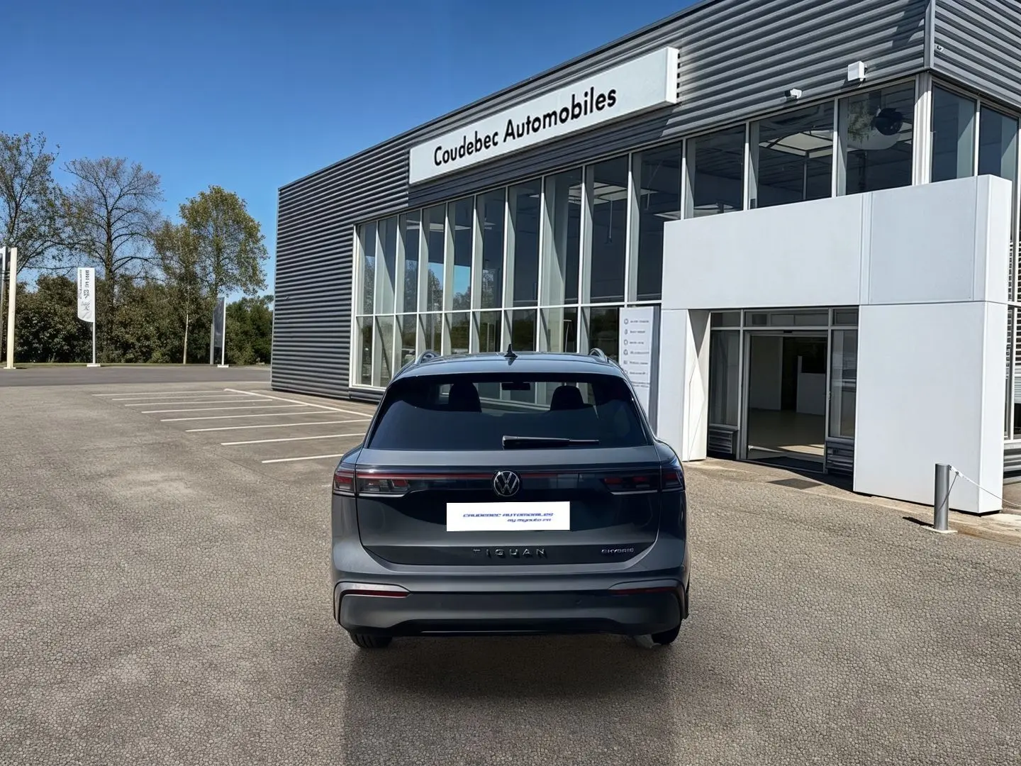 Vue arrière d'un Volkswagen Tiguan eHybrid gris stationné devant un bâtiment moderne de concession automobile.