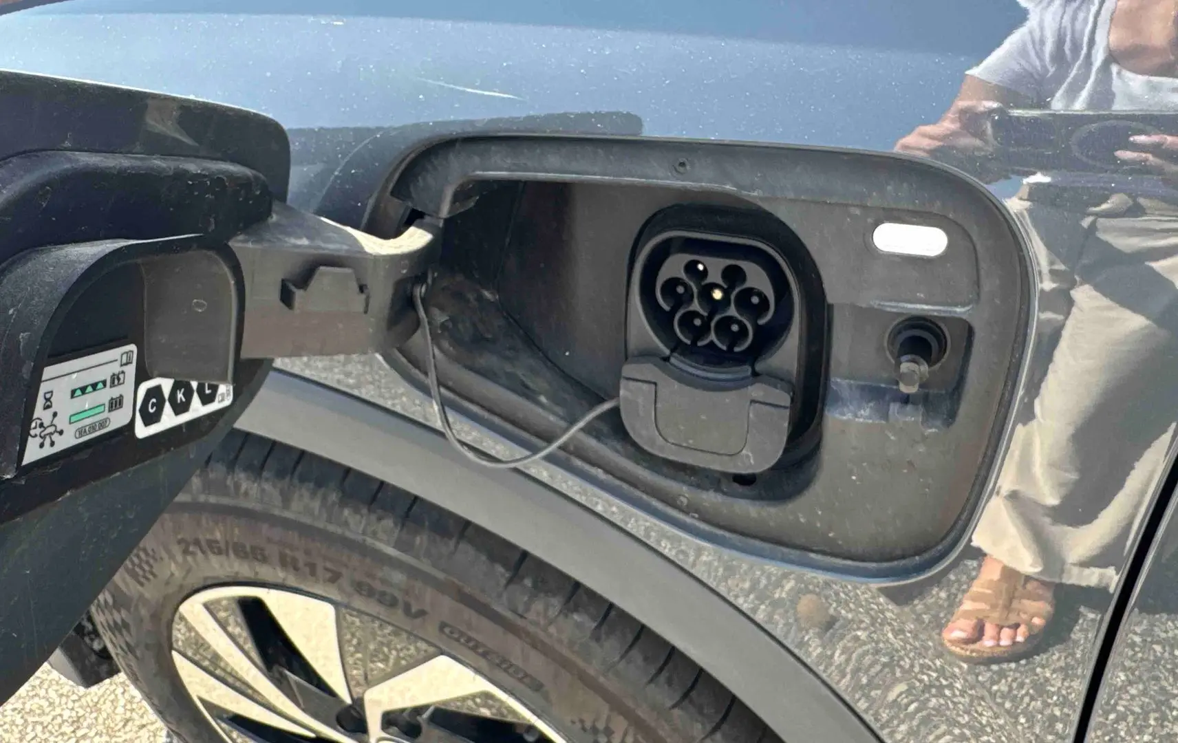Prise de recharge électrique ouverte côté gauche sur un Volkswagen Tiguan gris, avec jante alliage visible.