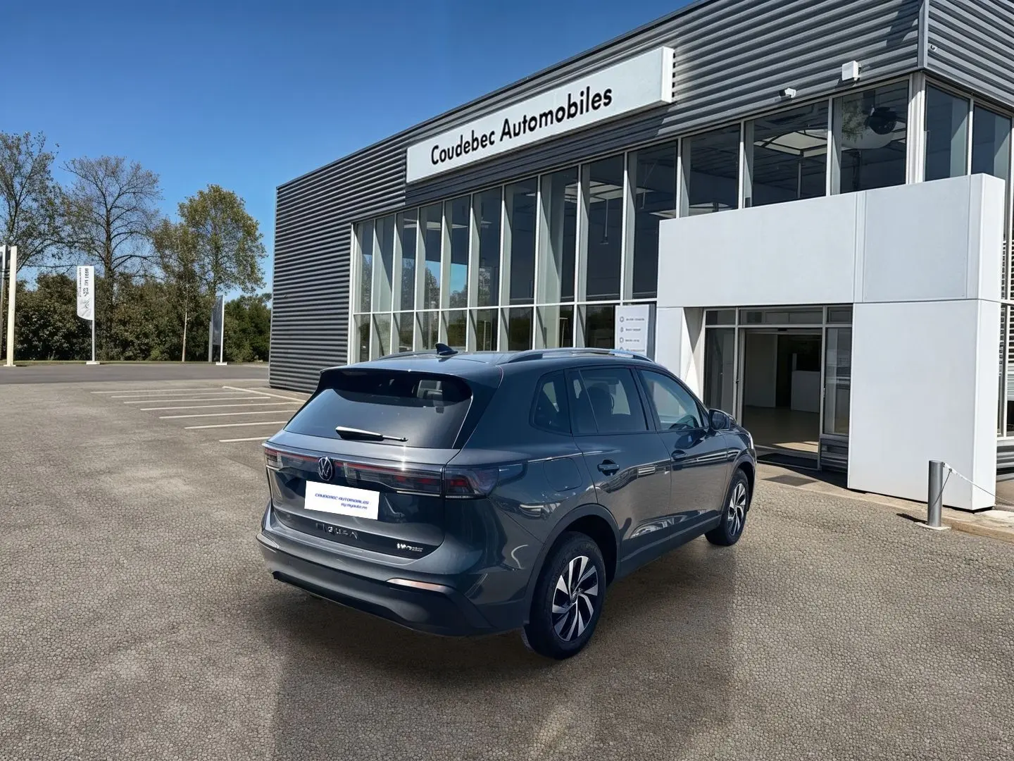 Vue 3/4 arrière droite du Volkswagen Tiguan eHybrid gris devant un bâtiment de concession Coudebec Automobiles.