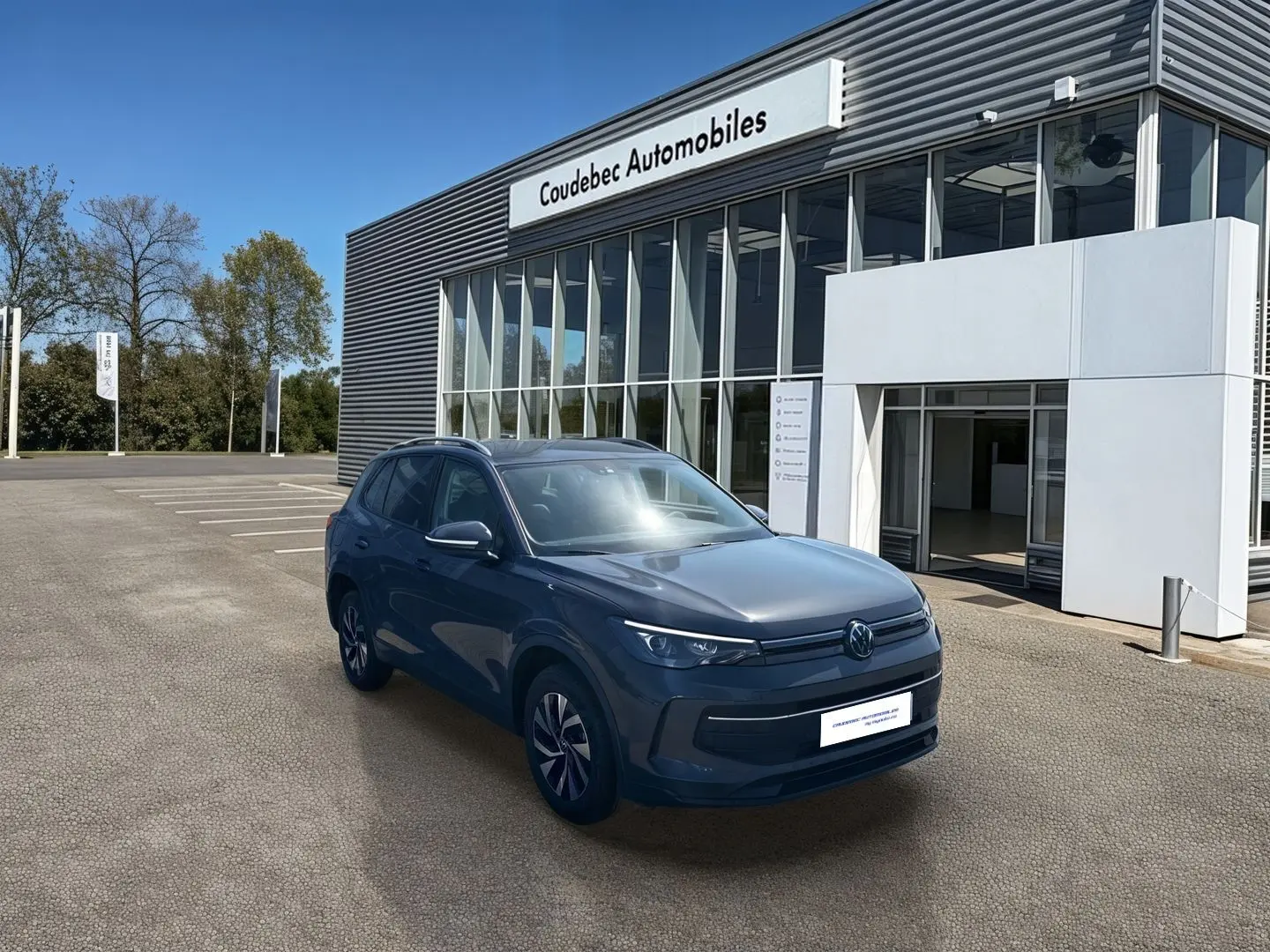 Vue 3/4 avant d'un Volkswagen Tiguan 1.5 eHybrid gris stationné devant un concessionnaire Coudebec Automobiles.