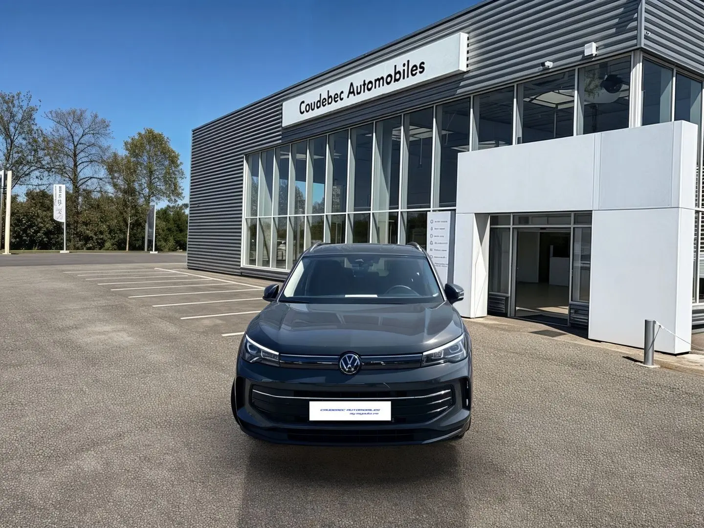 Vue avant d'un Volkswagen Tiguan 1.5 eHybrid gris stationné devant un bâtiment moderne de concession automobile.