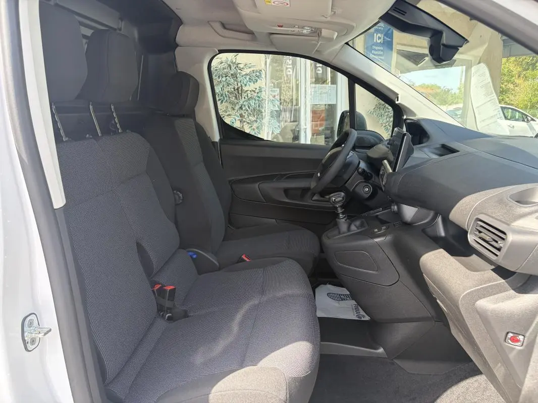 Vue intérieure côté conducteur du Peugeot Partner blanc 2026, montrant les sièges tissu, volant multifonctions et tableau de bord.