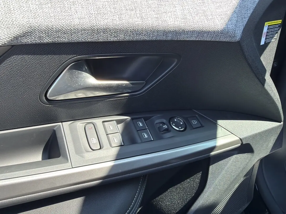 Gros plan sur la porte avant gauche noire du Peugeot 5008 2025, avec commandes électriques des vitres et poignée intérieure.