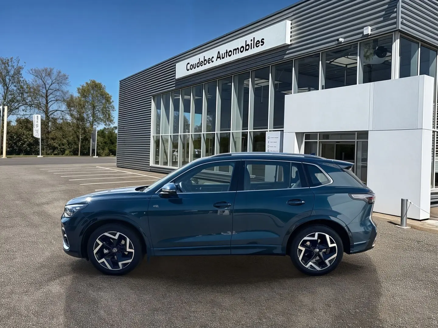 Vue latérale droite du Volkswagen Tiguan 2025 bleu, avec jantes alliage 19 pouces et finition R-Line devant un concessionnaire.