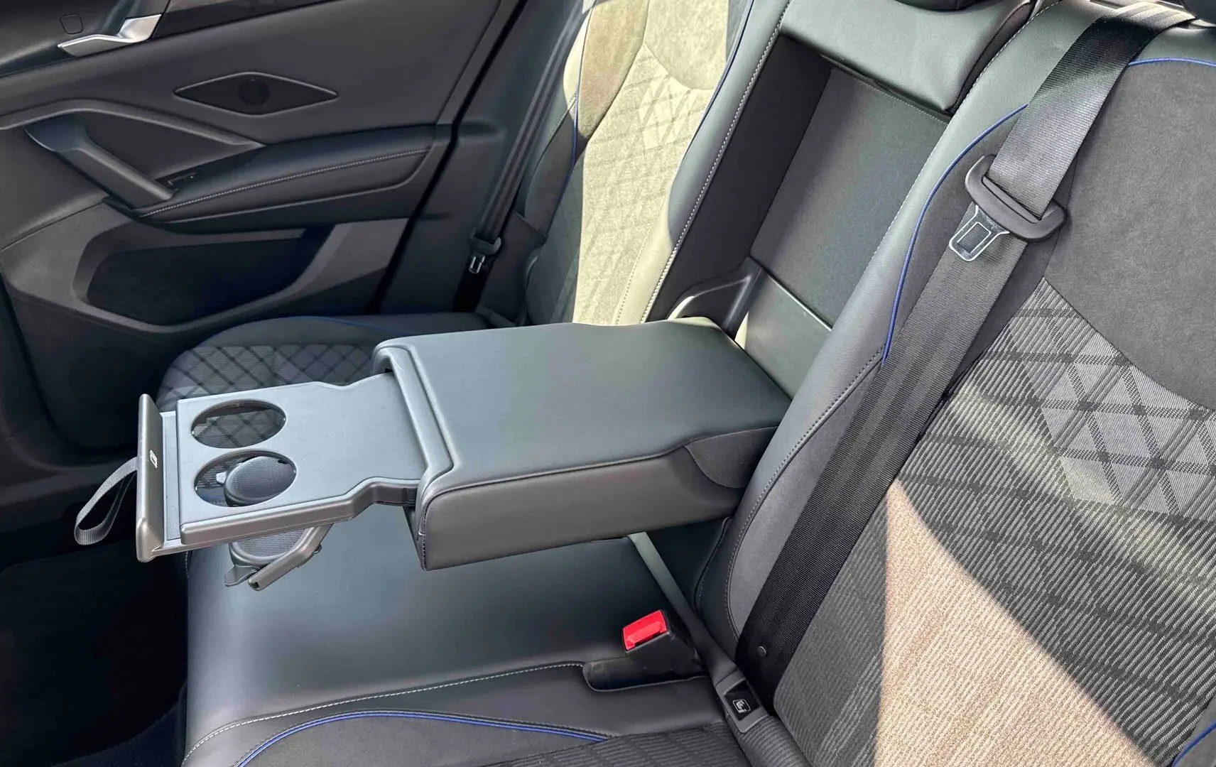 Vue intérieure arrière côté droit du Volkswagen Tiguan 2025, sièges noirs avec surpiqûres bleues et accoudoir central avec porte-gobelets.