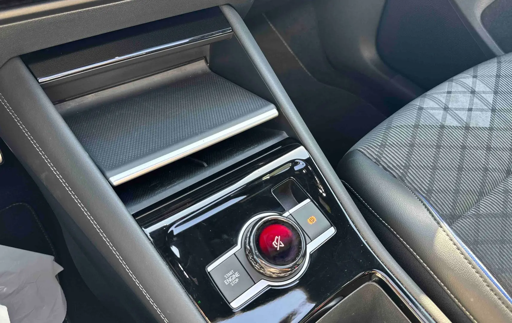 Gros plan sur la console centrale noire brillante du Volkswagen Tiguan 2025 avec bouton rotatif et siège tissu gris à motifs.