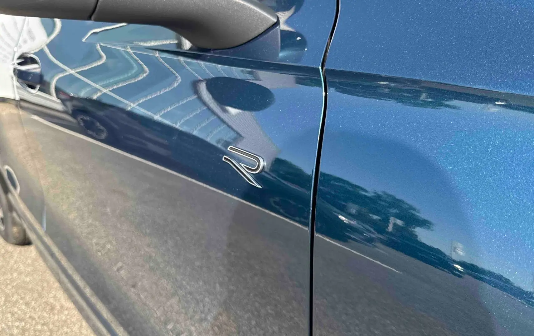 Gros plan sur la porte côté gauche du Volkswagen Tiguan bleu métallisé avec logo R distinctif.