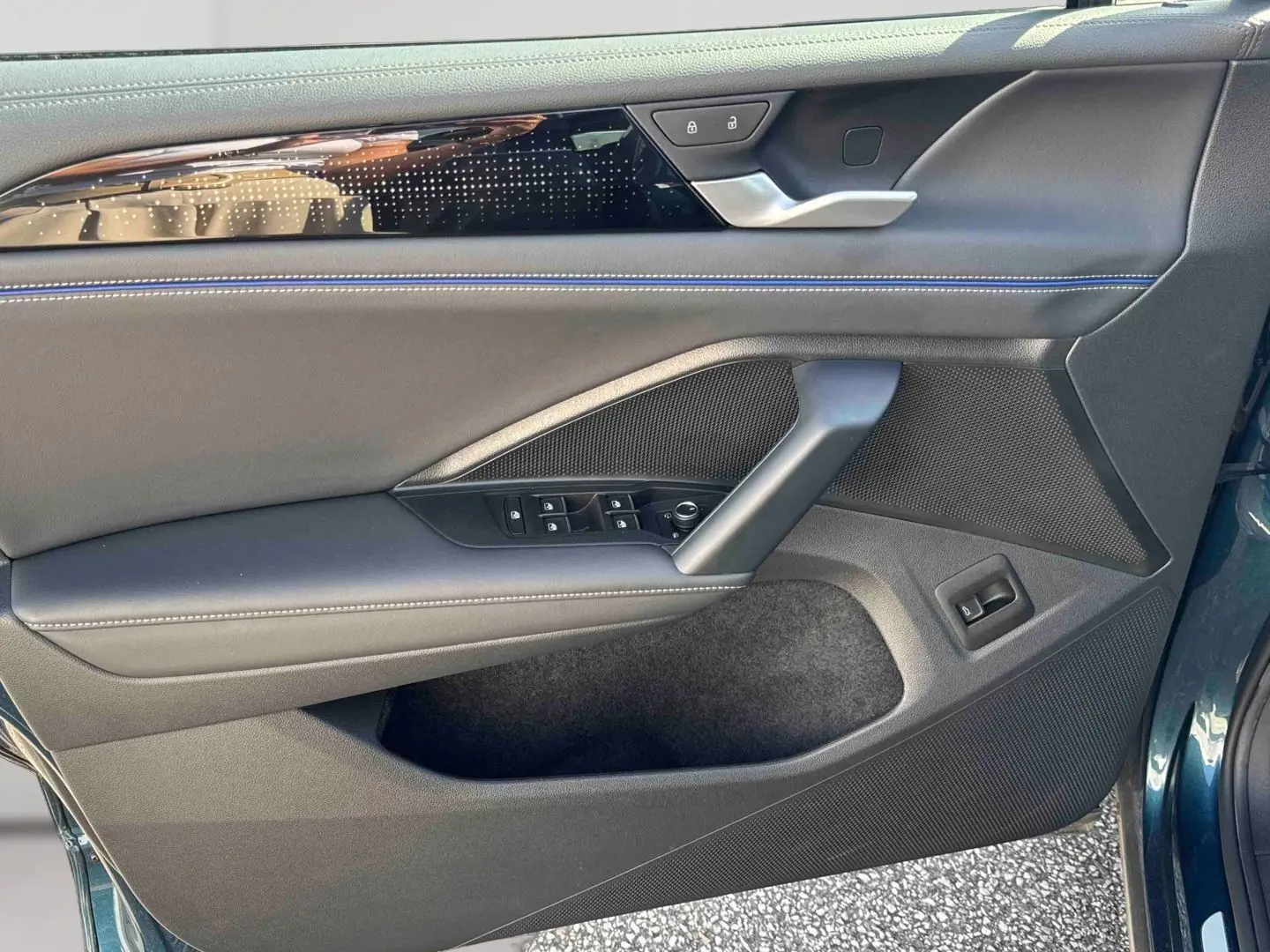 Vue rapprochée de la porte avant gauche du Volkswagen Tiguan 2025 bleu, avec garniture noire et surpiqûres bleues.