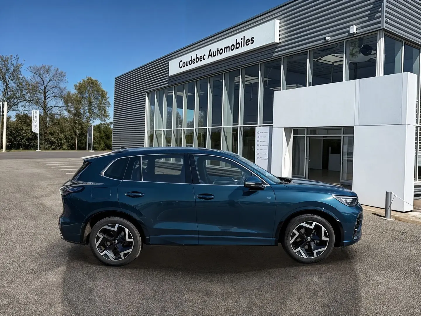 Vue de profil côté gauche d'un Volkswagen Tiguan 2025 bleu, avec jantes alliage 19 pouces et finition R-Line devant un concessionnaire.
