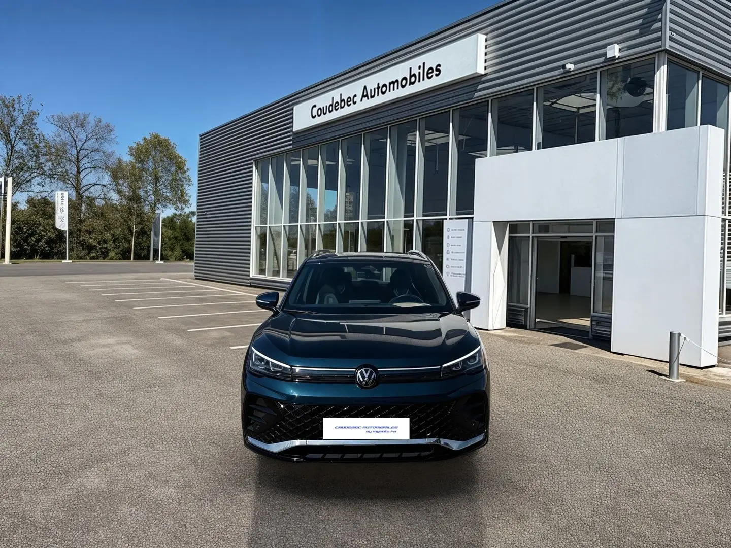 Vue de face du Volkswagen Tiguan 2025 bleu, avec calandre noire et phares LED, devant un showroom Coudebec Automobiles.