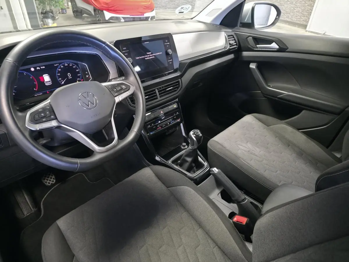 Vue intérieure côté conducteur du Volkswagen T-Cross 2025 avec volant cuir, tableau de bord digital et sellerie tissu gris.